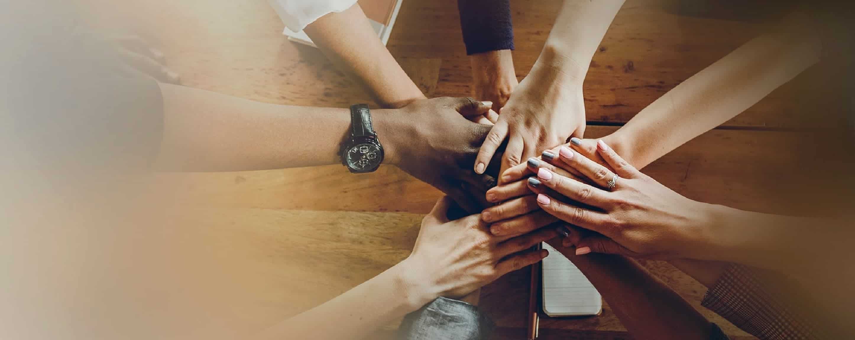 BIZ-LYNX Technology - A group of people place their hands on top of each other in a gesture of unity over a wooden table, showcasing their proven track record and exceptional customer service.