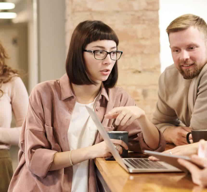 BIZ-LYNX Technology - Three people are gathered around a laptop on a wooden table. One person, holding a coffee mug, is pointing at the screen, discussing how their NGO can benefit from partnering with a top cloud service provider. Another person leans in, looking intently at the laptop as they review its proven track record.