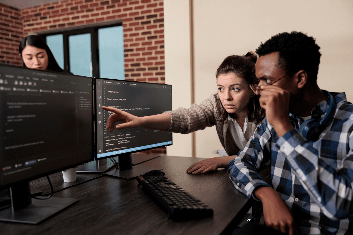 Two IT professionals analysing code on dual monitors in an office environment