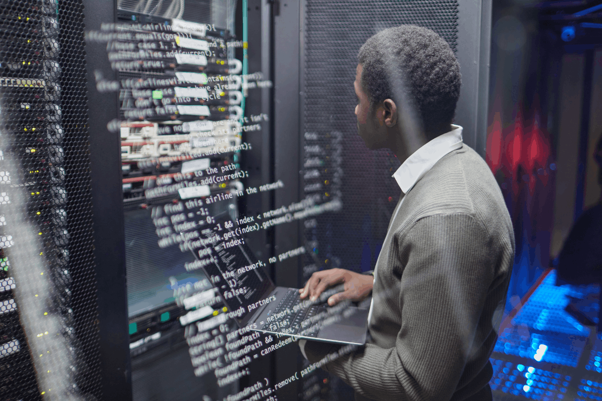 IT technician working on a laptop inside a server room with network equipment in the background