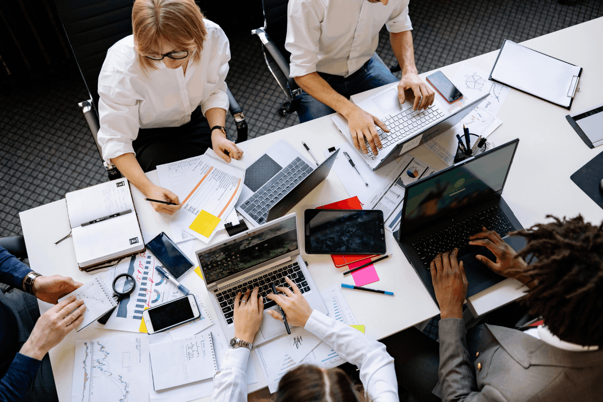 Overhead view of a team working together at a desk with laptops, documents and charts