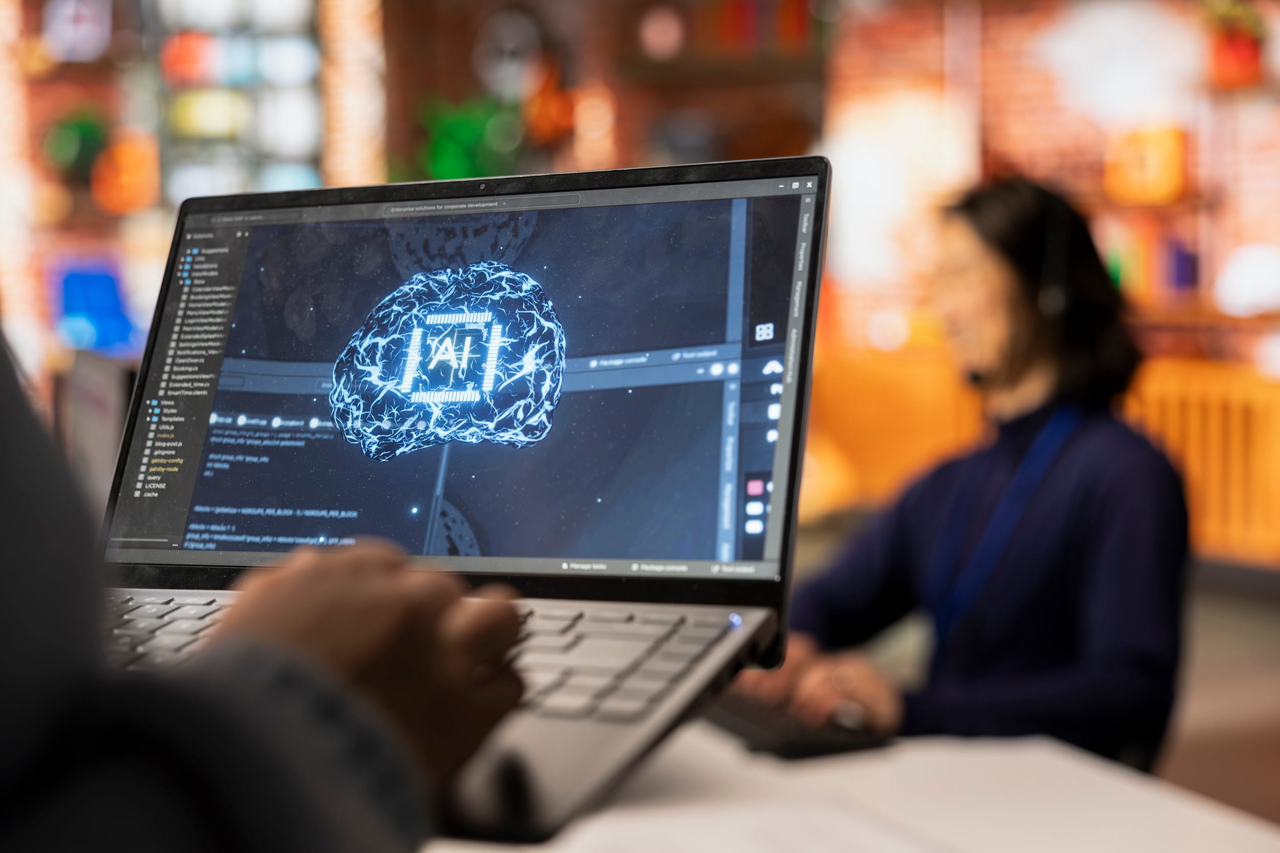 A laptop screen shows a glowing AI brain over lines of code, with a headset-wearing call centre worker blurred behind it.