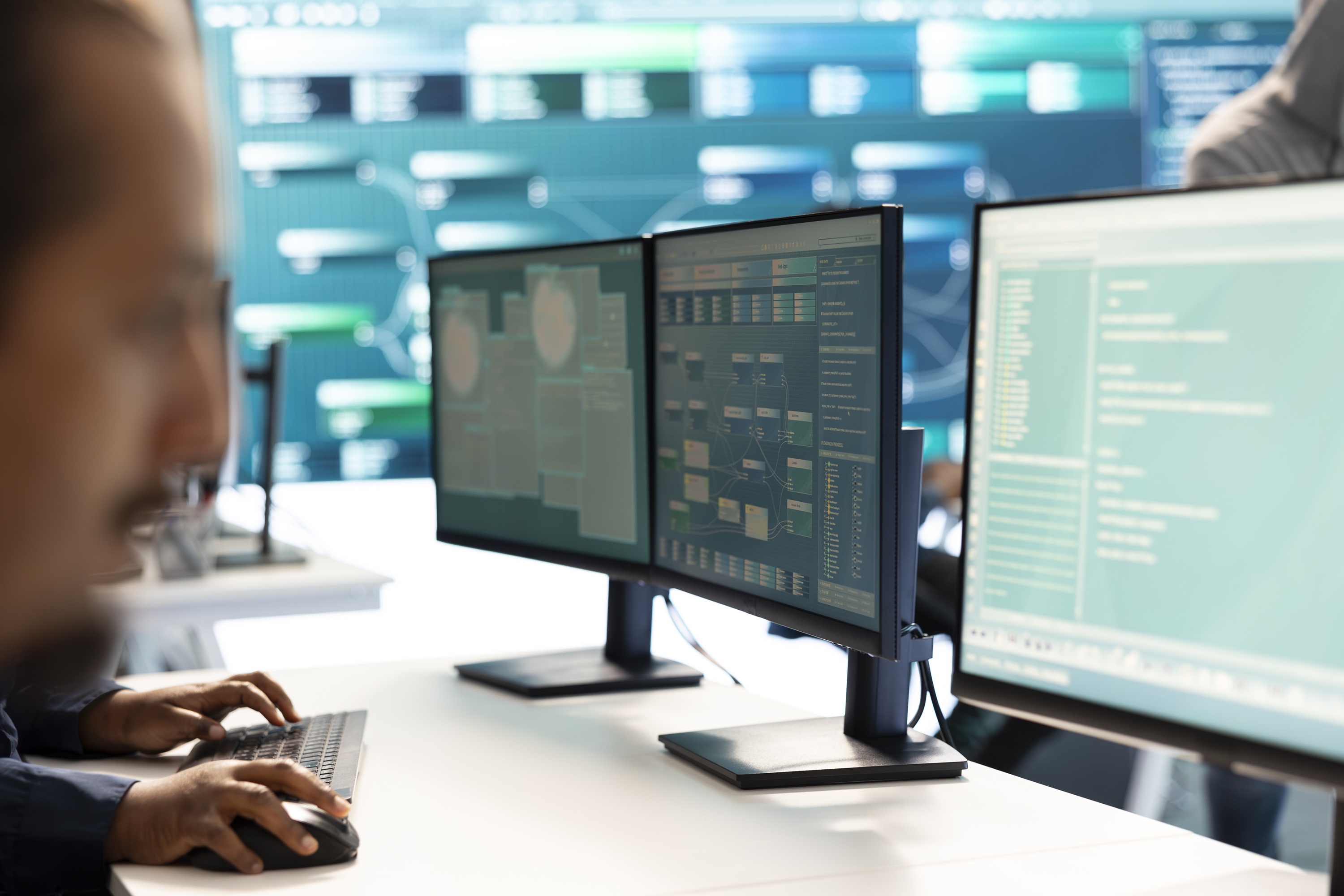 IT professional at a desk monitoring multiple computer screens displaying data dashboards, analytics, and system information.